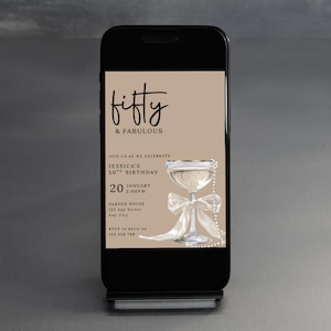 May include: A smartphone displays a digital invitation for a 50th birthday celebration. The invitation features the text "Fifty & Fabulous" in elegant script, a champagne glass, and event details. The background is a neutral beige.