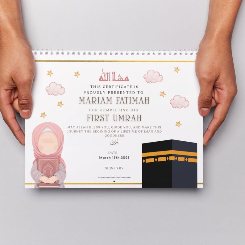 May include: A certificate with a spiral binding, held by hands. The certificate features text in English and Arabic, with illustrations of stars, clouds, and a Kaaba. The certificate is presented to Mariam Fatimah for completing her First Umrah.