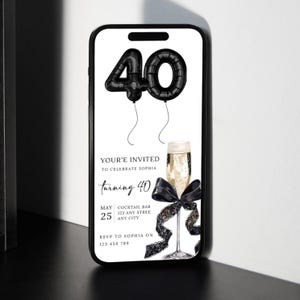 以下が含まれることがあります： スマートフォンには、40歳の誕生日のお祝いのデジタル招待状が表示されています。デザインは、黒い風船の数字40、シャンパングラス、黒いリボンが特徴です。招待状のテキストには「ソフィアの40歳のお祝いにご招待」と書かれています。