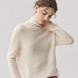 May include: A cream-colored turtleneck sweater paired with red and white checkered pants. The sweater has long sleeves and a soft texture. The pants have a drawstring waist. The outfit is casual and comfortable.