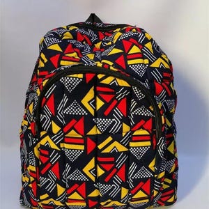 May include: A quilted backpack with a vibrant geometric pattern in red, yellow, white, and black. The backpack features a zippered main compartment and a smaller front pocket, with black zippers and a top handle.