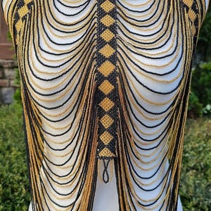 May include: A beaded body chain in black and gold. The necklace features a diamond pattern down the center and around the neck. The beaded strands cascade down the chest and back.