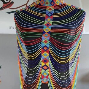 May include: A beaded necklace displayed on a black mannequin. The necklace features a high collar and a central panel with colorful geometric patterns. Strands of beads in various colors cascade down.