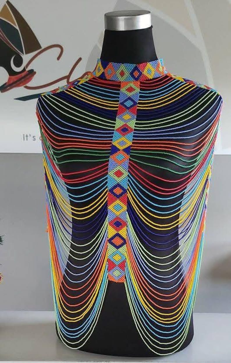 May include: A beaded necklace displayed on a black mannequin. The necklace features a high collar and a central panel with colorful geometric patterns. Strands of beads in various colors cascade down.