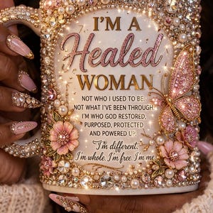 May include: White ceramic mug adorned with pink and gold embellishments, including pearls, rhinestones, and a butterfly. The mug features the text "I'M A Healed WOMAN" and inspirational quotes. A decorative and uplifting gift.
