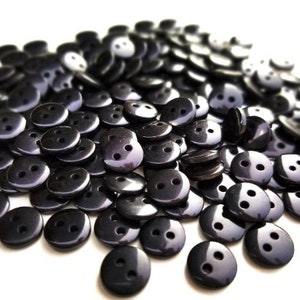 May include: A large pile of black plastic buttons with two holes each. The buttons are shiny and have a smooth surface.