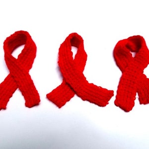 May include: Three red knitted ribbon loops, tied in a bow shape, on a white background.