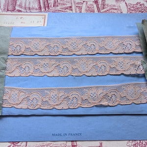 Peut inclure: Trois bandes de dentelle pêche délicate avec un bord festonné et un motif floral sont présentées sur un papier bleu clair. Le papier est étiqueté "MADE IN FRANCE" en bas. Une petite étiquette est attachée en haut à gauche.