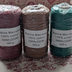 Può includere: Tre rocchetti di corda per macramè nei colori bordeaux, marrone e verde acqua. Ogni rocchetto è avvolto in plastica trasparente e ha un'etichetta con la scritta "Bobine Macrame 100% cotton 3MMx200M 380 g."