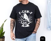 Photo 3 of 8: Black unisex crow pun tshirt with high-contrast white raven graphic perched on a skull framed by gnarled branches and bold F-CAW-F lettering, gothic crow shirt and skull bird tee with dark humor vibe, soft cotton fit styled with jeans, perfect edgy gift for men who love sarcastic tees