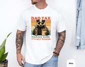 Photo 4 of 8: Model wearing a moss green garment dyed tee featuring a vintage badger cartoon — a badger dad tee design — holding fries and a drink with bold DAD TAX headline and cheeky "making sure it's not poison" line, soft washed casual funny dad shirt and dad tax shirt perfect Father's Day gift or novelty father gift