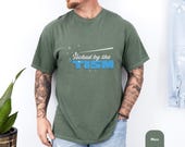 Photo 5 of 8: Moss green vintage wash tee with bold retro lettering that says touched by the tism, a funny autism shirt and neurodivergent shirt with cozy casual style for autism pride, mental health humor, or a thoughtful ASD awareness gift