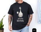 Photo 3 of 8: Folded charcoal unisex t shirt with a cheeky vintage goose sketch holding a coffee mug, a funny goose shirt and funny graphic tee with meme vibe and sarcastic charm, soft faded print on rustic wood backdrop, cozy novelty tee perfect gift for him or gift for dad with introvert humor