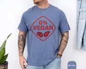 Photo 6 of 8: Blue jean soft cotton tee with a bold red 0% VEGAN steak graphic worn by a tattooed model, relaxed casual fit for summer grilling — a funny BBQ shirt and grilling tee ideal as a barbecue gift and meat lover gift, great as a grillmaster shirt or backyard BBQ tee for dad