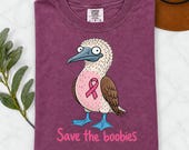 Photo 4 of 17: A folded maroon t-shirt with a cartoon blue-footed booby bird graphic, a pink ribbon, and the text Save the boobies.