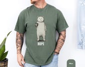 Photo 5 of 8: Charcoal unisex t shirt laid flat on rustic wood showing a hand-drawn bear clutching a coffee mug with the word NOPE beneath, a minimalist funny bear shirt mixing sarcastic t shirt and introvert humor, cozy coffee humor apparel and quirky gift for him