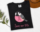 Photo 6 of 17: A folded black t-shirt displaying a cartoon bird graphic with a pink ribbon and text.
