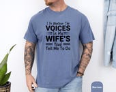 Photo 6 of 8: Unisex vintage wash blue jean shirt on a relaxed tattooed model, bold black quote reads I do whatever the voices in my wife's head tell me to do, soft worn-in feel, cheeky wife voices shirt and husband humor shirt ideal gag gift or funny marriage tee for married life
