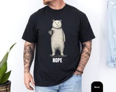 Photo 3 of 8: Male model in a soft muted blue unisex t shirt showing a deadpan bear holding a coffee mug with bold NOPE lettering, a funny bear shirt and bear graphic tee with minimalist, sarcastic t shirt vibe, cozy coffee humor and introvert gift idea for him