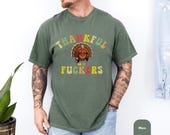 Photo 5 of 8: Man in cycling helmet leaning on a mountain bike on a leafy gravel path wearing a dark unisex humor tee with a cheeky Thanksgiving parody graphic and rude punchline, a playful inappropriate shirt with warm vintage colors and cozy fall vibe, perfect friendsgiving shirt and funny thanksgiving gift for friends