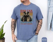 Photo 6 of 8: A man wearing a garment dyed tee with a retro badger dad illustration and playful dad tax joke, leaning on a mountain bike on a sunlit trail, cozy soft washed look and casual fit, perfect funny dad shirt and Father's Day gift idea
