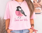 Photo 3 of 17: A person wearing a light pink t-shirt printed with a bird wearing a pink ribbon and the words Save our tits.