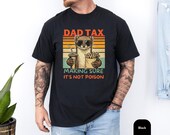 Photo 3 of 8: Man modeling a garment dyed pepper unisex dad shirt with a cheeky weasel character tee holding fries and a drink against retro sunset stripes, vintage faded look and bold Dad Tax slogan, a funny dad tee and novelty dad gift ideal as a Father's Day shirt