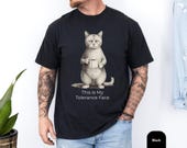 Photo 3 of 8: Folded charcoal unisex tee featuring a vintage halftone grumpy cat holding a coffee mug, muted sepia print on soft cotton for a cozy worn-in feel, styled on rustic wood with customer review badges, a funny cat shirt and cat meme shirt that's a sarcastic t shirt dry humor novelty cat tee gift for him or cat owner