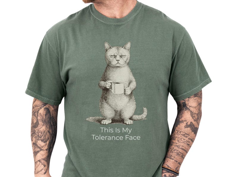 Moss green unisex t shirt on a tattooed male model featuring a vintage grumpy cat holding a coffee mug with the caption This Is My Tolerance Face, a funny cat shirt and cat meme tee with dry, sarcastic humor, cozy soft feel, novelty cat tee and cat lover gift for him
