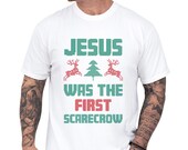 Photo 2 of 7: Black unisex cotton Christmas T-shirt with cozy pixel-style green and red print reading Jesus was the first scarecrow, reindeer and tree accents, a funny Christmas tee and funny religious tee that's cheeky and slightly inappropriate, perfect gift for him or her and casual holiday outfit
