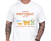 Photo 2 of 10: Male model wearing a white unisex funny shirt with bold orange pixel text saying please be patient with me i was born in the 1900s, retro pixel art wagon, bison and mountain scene in blue and green, cozy gamer style tee and novelty joke tshirt, great old school humor gift for Gen X or millennial birthdays