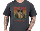 Photo 1 of 8: Charcoal garment-dyed unisex dad weasel shirt with a soft worn-in feel, featuring a cheeky weasel in sunglasses holding fries and a soda against vintage sunset stripes, bold DAD TAX humor and "making sure it's not poison" copy, funny dad tee and novelty Father's Day gift idea for proud dads
