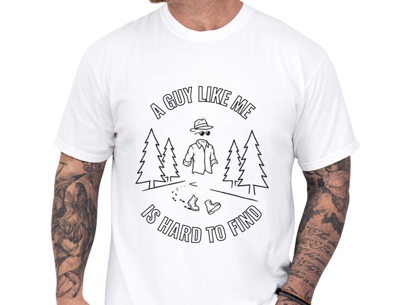 Soft moss Comfort Colors cotton tee worn by a man, sarcastic dad joke tee that reads "A guy like me is hard to find" with invisible man sketch, pine trees and boots, punny graphic humor cotton shirt ideal for casual weekend wear or Father's Day gift