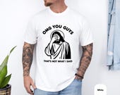 Photo 4 of 8: White unisex funny tshirt worn by a tattooed male model featuring a bold black meme graphic of Jesus doing a facepalm with text OMG YOU GUYS and "That's not what I said" — a sarcastic jesus facepalm tee, vintage wash style novelty joke shirt and gift for christians