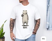 Photo 4 of 8: Folded charcoal unisex t shirt with a minimalist hand drawn bear holding a coffee mug and a deadpan nope vibe, cozy vintage wash and soft texture visible, a funny bear shirt for introvert humor and coffee lovers, minimalist humor tee and sarcastic novelty graphic tee gift for him