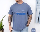 Photo 6 of 8: Cozy vintage wash tee in soft blue with a bold sarcastic humor print reading touched by the tism, styled on a relaxed model for a fun funny autism shirt, neurodivergent shirt, and thoughtful ASD awareness gift