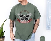 Photo 5 of 8: Funny introvert tee in soft moss green, styled on a tattooed model with a bold butterfly graphic and anti social lettering for a cool vintage style tee, unisex funny shirt, and thoughtful gift for introverts who love edgy humor and relaxed everyday style