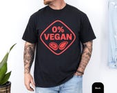 Photo 3 of 8: Man wearing a black, soft cotton tee with a bold red '0% VEGAN' badge and steak icons, a playful funny BBQ shirt and grilling tee for the grillmaster — cozy, casual BBQ style ideal as a meat lover gift, backyard bbq tee or gift for dad