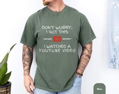 Photo 5 of 8: Man in bike helmet leaning on a mountain bike on a leafy gravel path wearing a funny dad tee with retro play icon and YouTube repair joke, soft cotton fabric in comfort dye colors, cozy fit perfect as a Father's Day present or birthday gag gift for a garage project dad