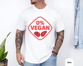 Photo 4 of 8: White casual tee on a bearded, tattooed man featuring a bold red diamond reading "0% VEGAN" with steak icons, cheeky and playful funny BBQ shirt perfect as a grilling tee or meat lover gift, great barbecue gift or grillmaster shirt for backyard bbq and gift for dad