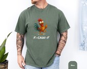 Photo 5 of 8: Male cyclist in helmet and sunglasses leans on a mountain bike on a tree-lined gravel trail wearing a faded olive Comfort Colors graphic tee with a cheeky middle finger chicken and f caw f text, a funny edgy protest statement tee and adult humor tee for casual streetwear, cozy relaxed fit, great gift for him or gift for dad, men's gift ideas