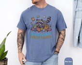 Photo 6 of 14: Male model wearing a soft blue-jean unisex t shirt featuring a colorful raccoon graphic tumbling through snacks with a cheeky Trash Panda slogan, playful and slightly sarcastic, a cute raccoon shirt that doubles as a funny animal tee, raccoon graphic tee, novelty graphic tee, humor t shirt, perfect animal lover gift or cool gift for him