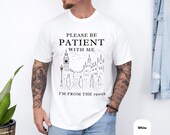 Photo 4 of 8: Charcoal vintage-style sarcastic t shirt laid flat on rustic wood with light gray skyline illustration and the phrase please be patient with me i'm from the 1900s, a cozy millennial and gen x novelty graphic tee and funny saying tee perfect as a dad gift grandfather shirt or gift for husband