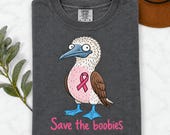 Photo 7 of 17: A folded dark gray t-shirt with a cartoon blue-footed booby bird graphic, pink ribbon, and Save the boobies text.