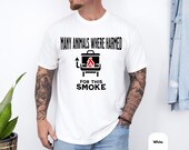 Photo 4 of 8: Male model in a white casual tee with a cheeky grill graphic and slogan about animals harmed for this smoke, bold black lettering with a small red flame, relaxed fit with jeans and tattoos, cozy backyard barbecue vibe, ideal bbq humor shirt, dark humor tee and funny grill shirt, a sarcastic bbq tee or grillmaster shirt style perfect as a meat smoker gift for a grilling enthusiast or dad grill shirt