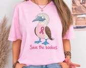 Photo 3 of 17: A woman standing and wearing a pink t-shirt printed with a blue-footed booby bird graphic and the text Save the boobies.