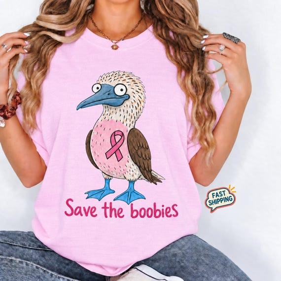 A woman wearing a pink t-shirt featuring a cartoon blue-footed booby bird with a pink ribbon and the text Save the boobies.