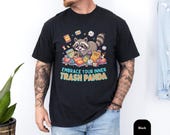 Photo 3 of 14: Casual model wearing a black unisex trash panda shirt featuring a playful raccoon graphic diving into snacks and bright cheeky lettering 'Embrace Your Inner Trash Panda', a funny animal tee, sarcastic shirt and raccoon t shirt — cute novelty gift for animal lovers and cool gift for him