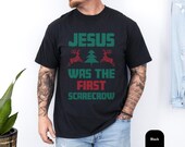 Photo 1 of 7: Funny christian tee with a black shirt and retro holiday graphic reading Jesus was the first scarecrow, styled like a cozy ugly sweater style design with festive reindeer and tree details, perfect christian gift shirt or gag gift shirt for Christmas laughs