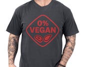 Photo 1 of 8: Charcoal vintage soft cotton tee with bold distressed red 0% VEGAN diamond graphic and steak icons, shown on a casually tattooed model — a funny BBQ shirt and grilling tee for backyard cookouts, ideal meat lover gift, grillmaster shirt and casual BBQ tee or gift for dad